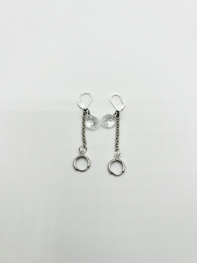  a pair of silver leverback earrings featuring a clear glass bead dangling from the post, with a chain and circular earring post at the base are laying flat on a white background.