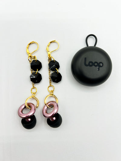 Gold leverback earrings featuring two black glass beads dangling from the post, with a chain and circular earring post at the base. These earrings also include pink LOOP earplugs fastened inside the clasp, providing both style and hearing protection.