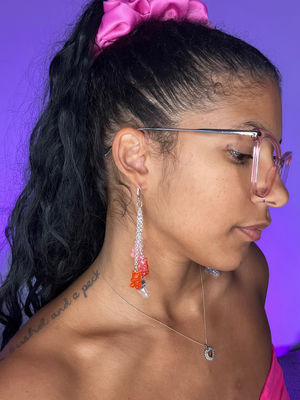 Purple Background. Black woman facing the right wearing high fidelity ear plug earrings in silver with Gummie bears dangling