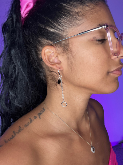 Purple Background. Black woman facing the right wearing LOOP Ear plug Earrings in silver with a black bead