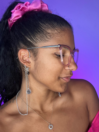 Purple Background. Black woman facing the right wearing over the ear high fidelity ear plug earrings in silver with a Black bead.