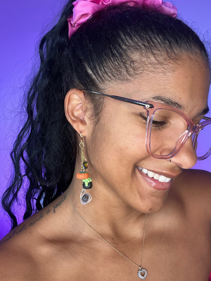 Purple Background. Black woman facing the right wearing  high fidelity ear plug earrings in gold with clay charms dangling