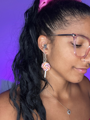 Purple Background. Black woman facing the right wearing silver high fidelity ear plug earrings with clay charms of Lollipops
