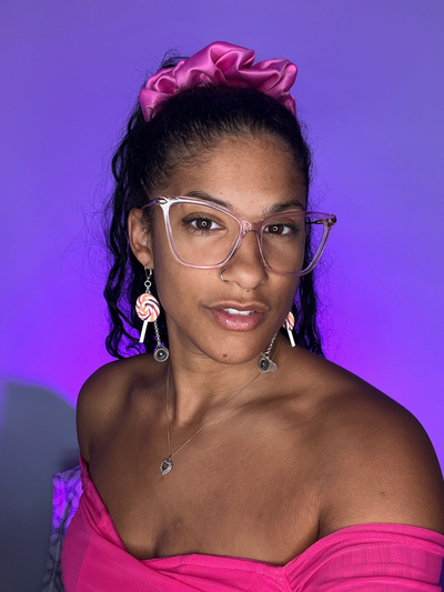 Purple Background. Black woman facing the right wearing silver high fidelity ear plug earrings with clay charms of Lollipops