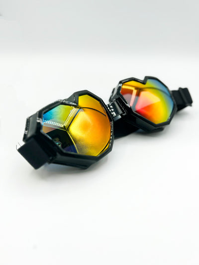 There is a White background. The LoveGaze Rave Goggles in black are displayed. the goggles are heart shaped and have a mirrored lense on them that colour shifts from blue, to green, to yellow, to orange, to red.
