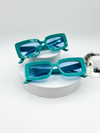 A white background with two pairs of the same sunglasses. Our PopBlocks sunglasses are rectangular shaped with thick bright and colourful frames, with lenses that match. this pair is a bright blue.