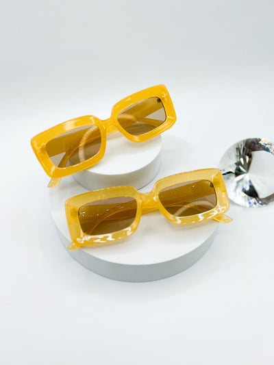 A white background with two pairs of the same sunglasses. Our PopBlocks sunglasses are rectangular shaped with thick bright and colourful frames, with lenses that match. this pair is a bright Yellow with very light brown lenses..